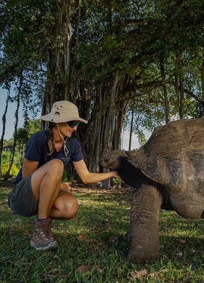 A visitor greeting a giant Aldabra tortoise on the island's lawn