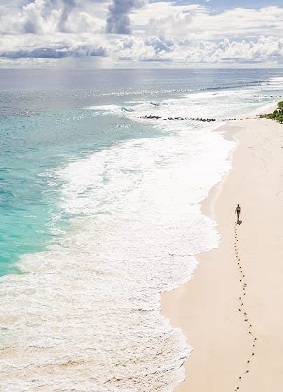 A person walking along a long, empty white-sand beach beside turquoise surf