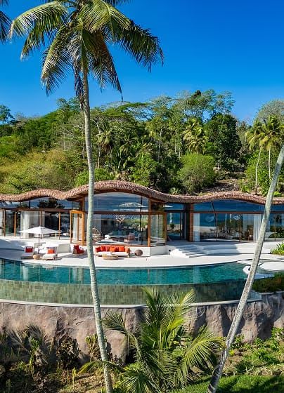 A luxury villa with a curved roof and infinity pool set into tropical gardens