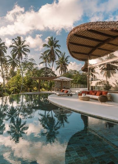 A villa infinity pool beside a thatched pavilion, palms reflected in the water at sunset