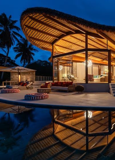 A curved timber-roofed villa glowing at dusk, mirrored in its reflecting pool