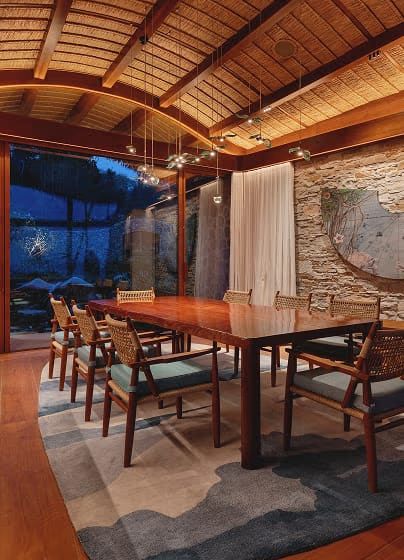 A villa dining room with a long wooden table and chairs beneath a warm timber ceiling