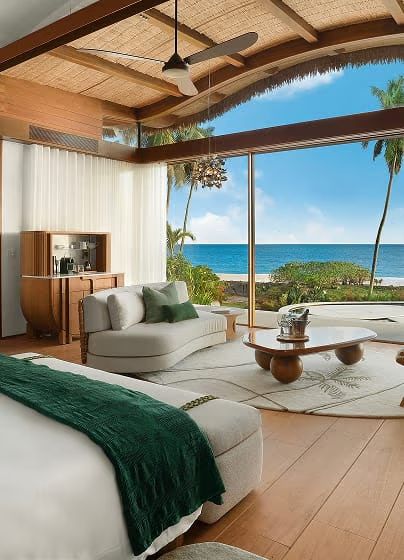 A villa bedroom opening onto ocean and palm views through full-height windows